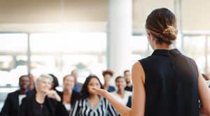 An audience is listening and engaged with a great speaker presenting and delivering great leadership. Business Impact article image for the art of being heard.