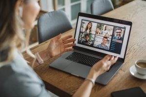 Business Impact article on creating a high-performing hybrid workplace: what should leaders do? A person is having a remote team meeting on the laptop. The individual is working from home engaging with peers. Next to her laptop sits a small shot of espresso.