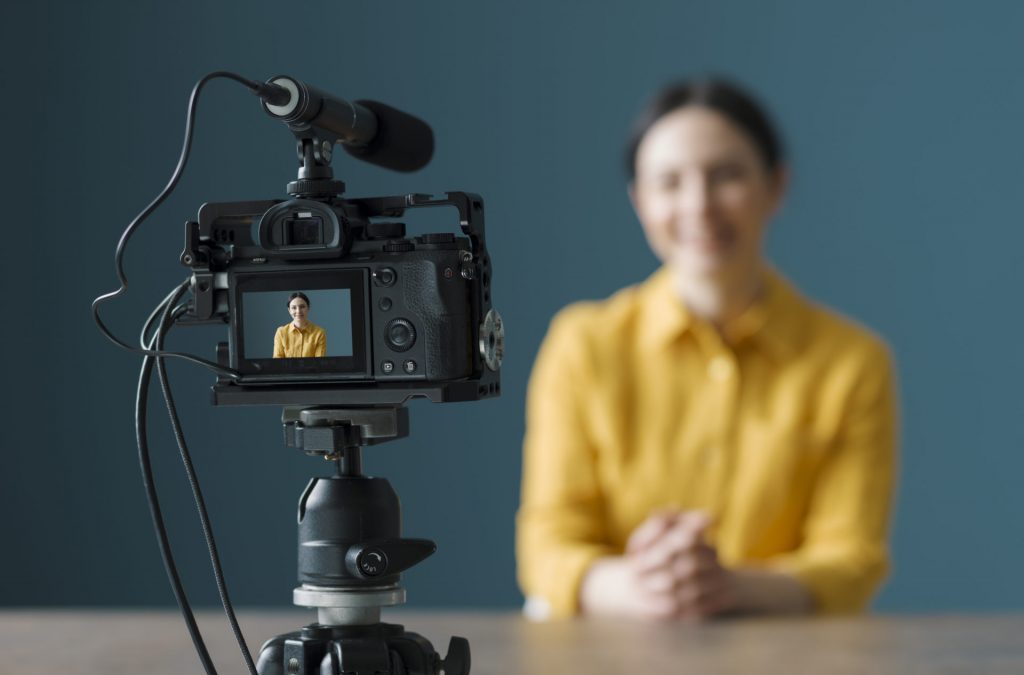 Smiling woman sitting in front of a camera and making a video blog. BGA Media Enquiries