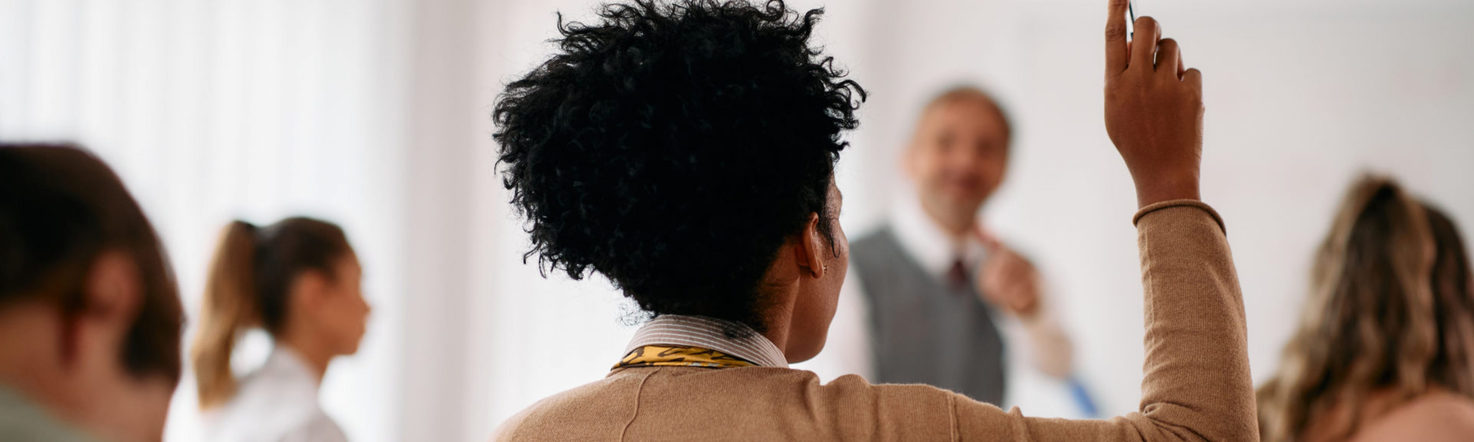 Back view of African American student raising her arm to answer a question during lecture in the classroom.