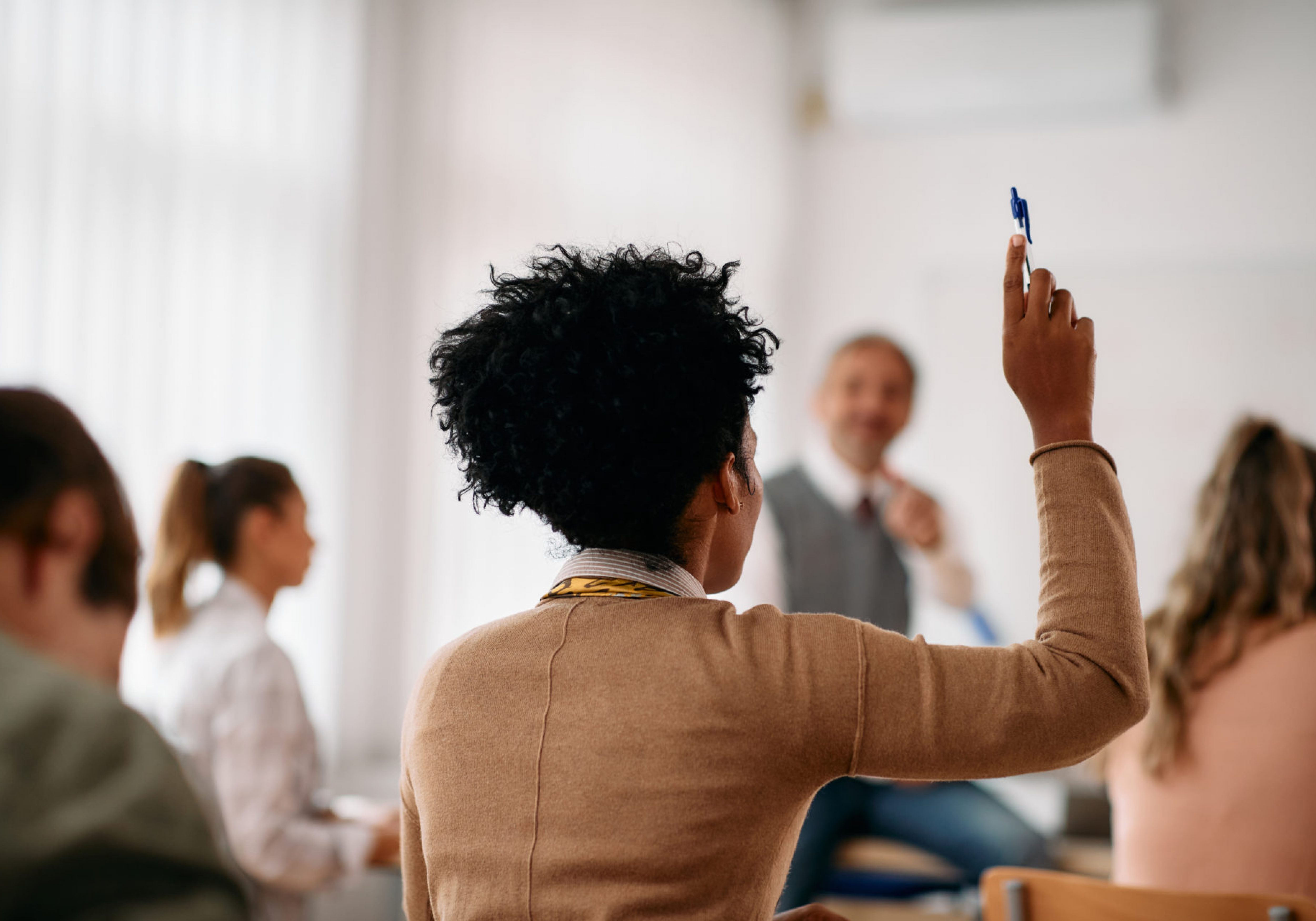 Back view of African American student raising her arm to answer a question during lecture in the classroom.