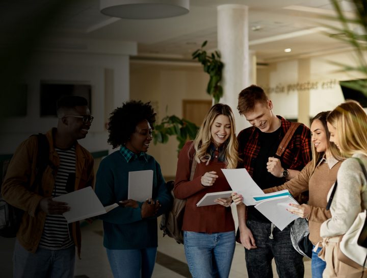 Group of happy students looking at exam results while standing at university hallway.