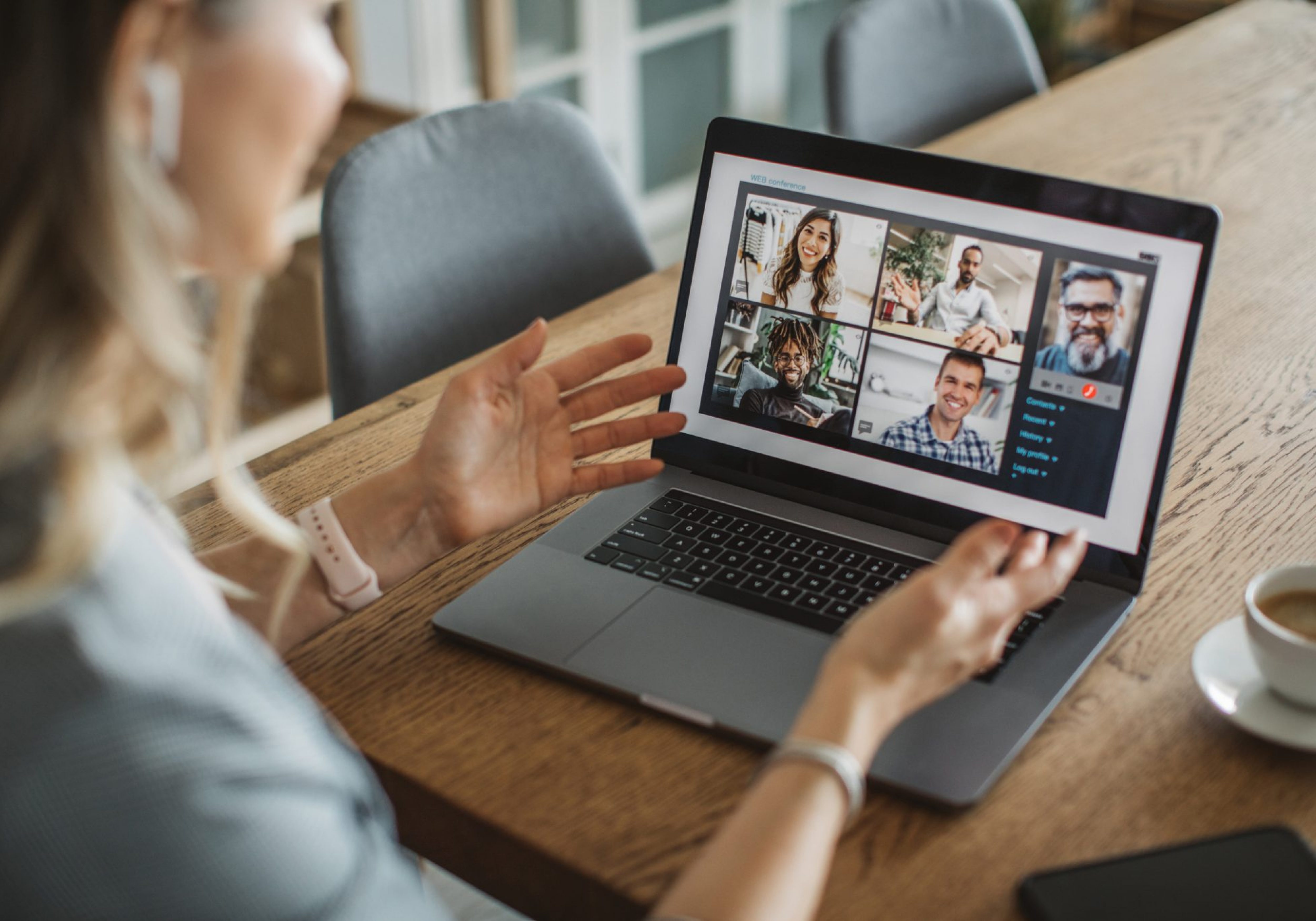 Business Impact article on creating a high-performing hybrid workplace: what should leaders do? A person is having a remote team meeting on the laptop. The individual is working from home engaging with peers. Next to her laptop sits a small shot of espresso.